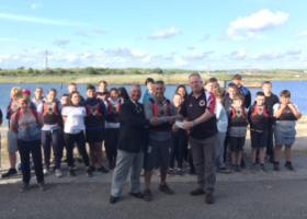 Mr Peter Fisher and Mr Ken Collins presenting a cheque to Mr Jason Zacharini, with members of the Barrow Sea Cadet Sailing Centre in the background