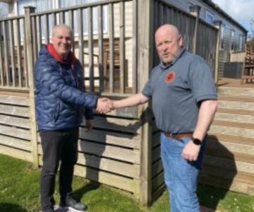 Mick shaking hands with man in blue puffa jacket in front of a large static carvan